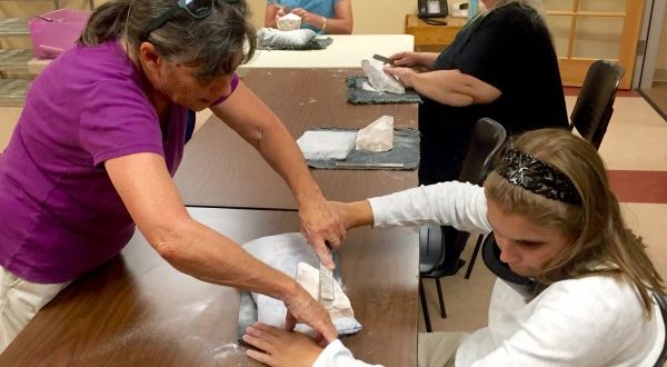 Two women practice the use of a file on a white stone
