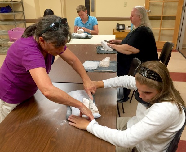 Two women practice the use of a file on a white stone