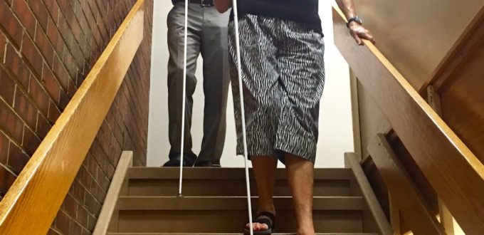 A young man gives a senior woman a cane lesson on the stairs