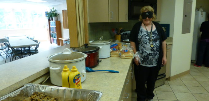Woman wearing sleepshades stands beside a row of hotel pans filled with food