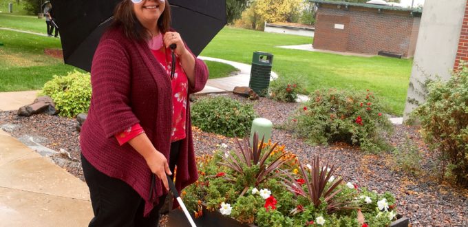 A woman wearing sleep shades returns to the Center with her white cane in one hand and umbrella in the other