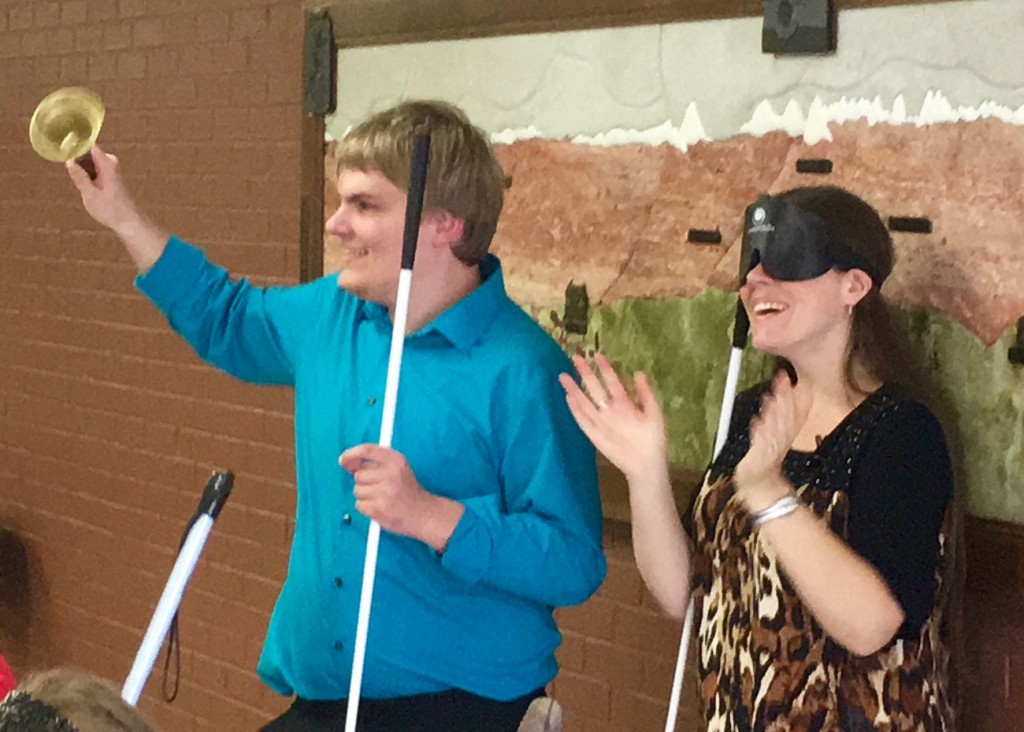 Man holding his bell high as he rings it, a woman stands beside him applauding