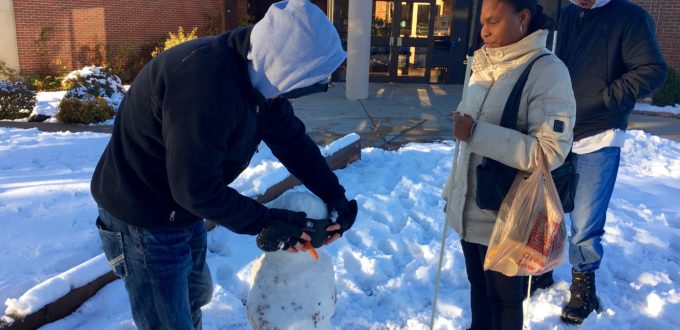 Two men and a womanadd sleepshades and white cane to their snow person that has a carrot nose.