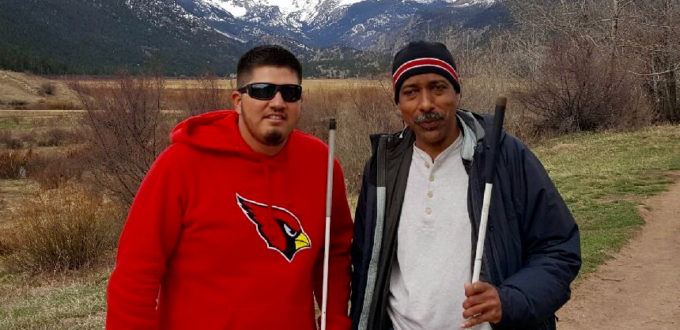 Two men grin at the camera with snowy mountains behind them
