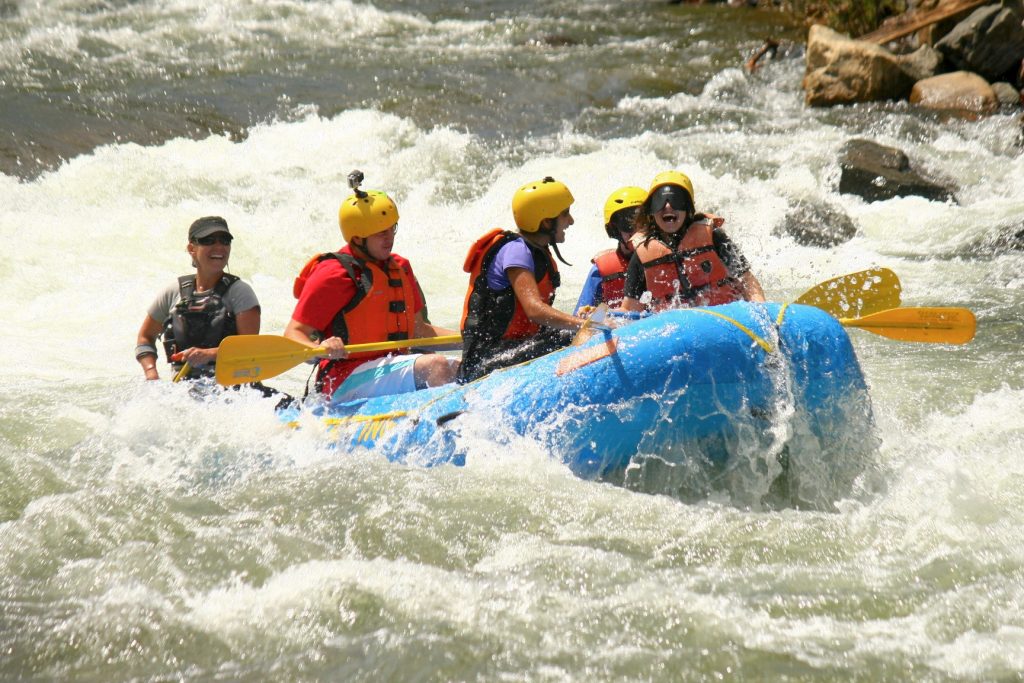 The front of the raft lifts up high as swirling white water splashes all around