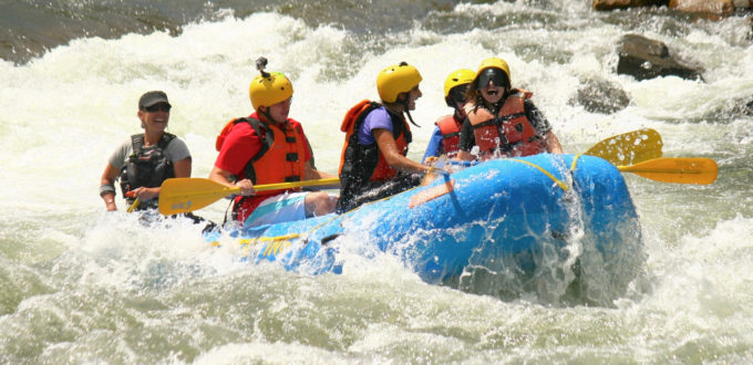 The front of the raft lifts up high as swirling white water splashes all around