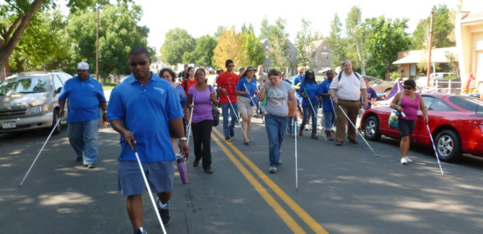 a group of people carrying white canes walk down the middle of a street