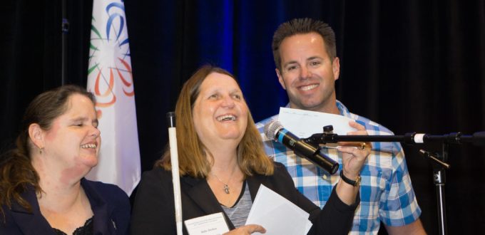 Marc Greytak presents check to Julie Deden at podium, Maryann Migliorelli looks on
