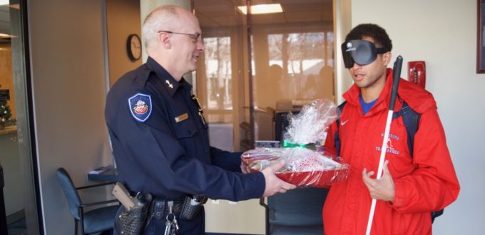 Chaz presents a Christmas basket of items prepared by CCB students to an officer from the Littleton Police Department