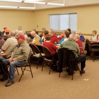 Duncan stands in front of a large group of Seniors at the CCB Christmas party while people introduce themselves