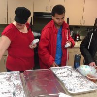 Libby, Chaz and Chip get breakfast burritos out of huge trays in the large kitchen