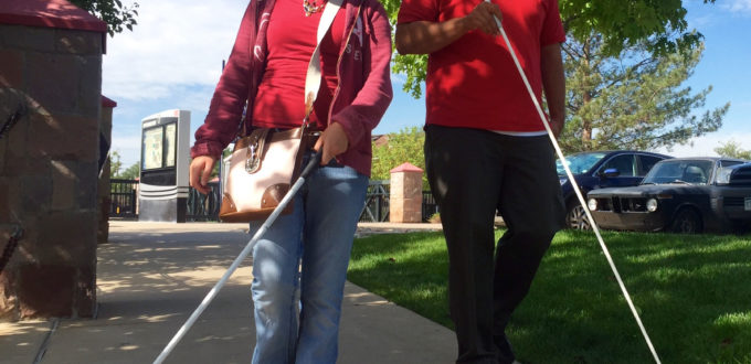 Vika and Martin walk along a shaded sidewalk toward Littleton Downtown Station