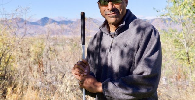 Warren standing with his cane outside the Center with the Mountains in the Background