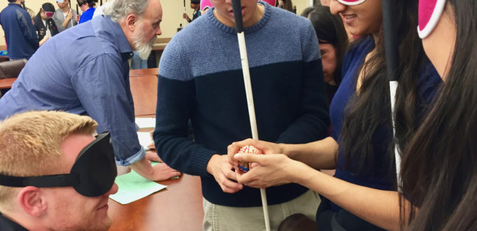 Students in sleepshades examine the mode of a brain on the table between them