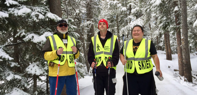 Three people wearing snow shoes on a wintery forested path with snow covered branches.