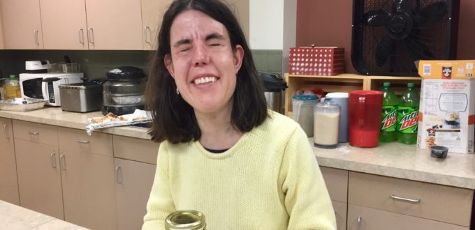 a smiling young woman holds a quart jar of amber appplesauce