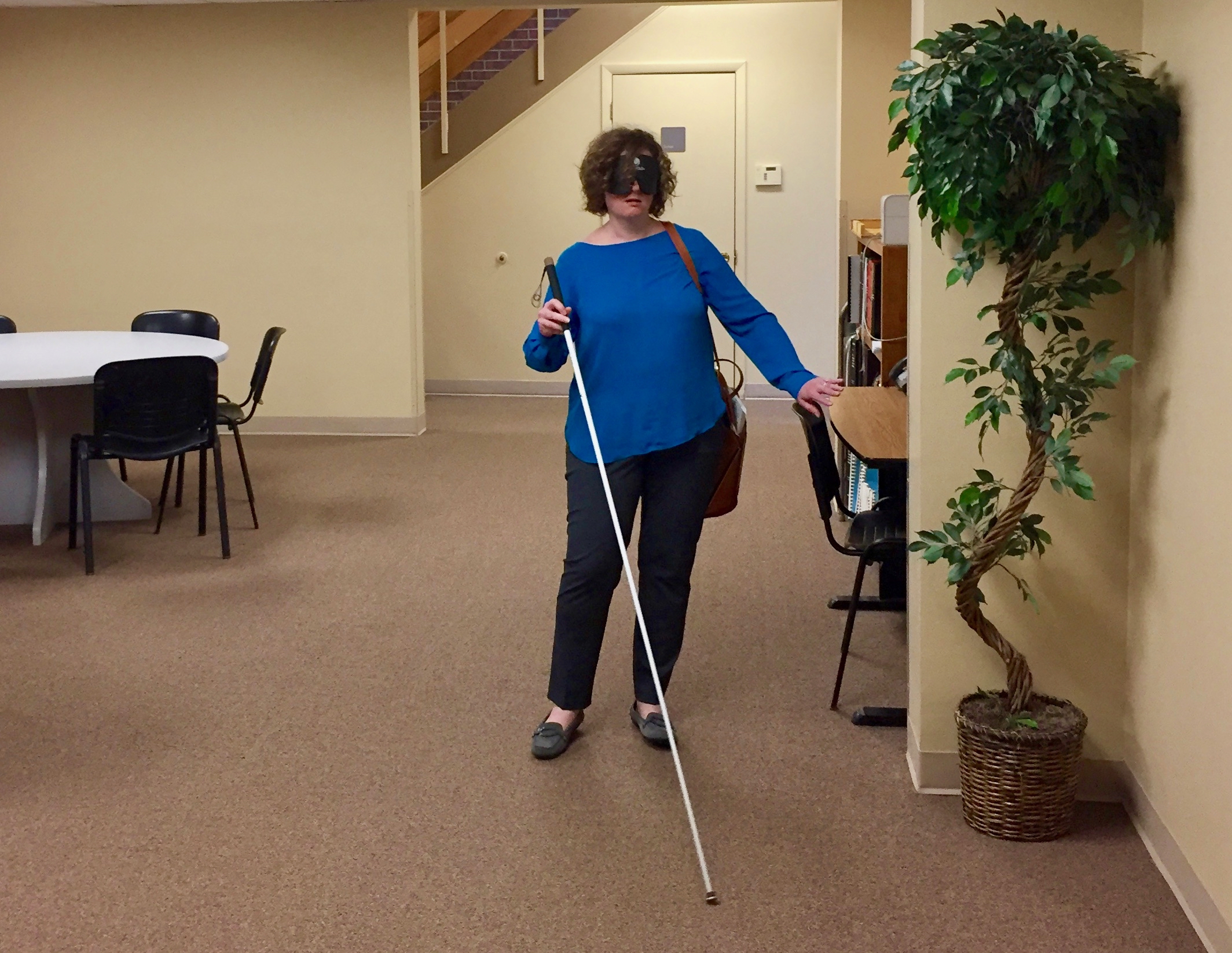 a woman wearing sleep shades uses her cane to maneuver in the Travel Lobby.