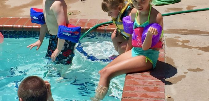 two little girls dangle feet into the pool