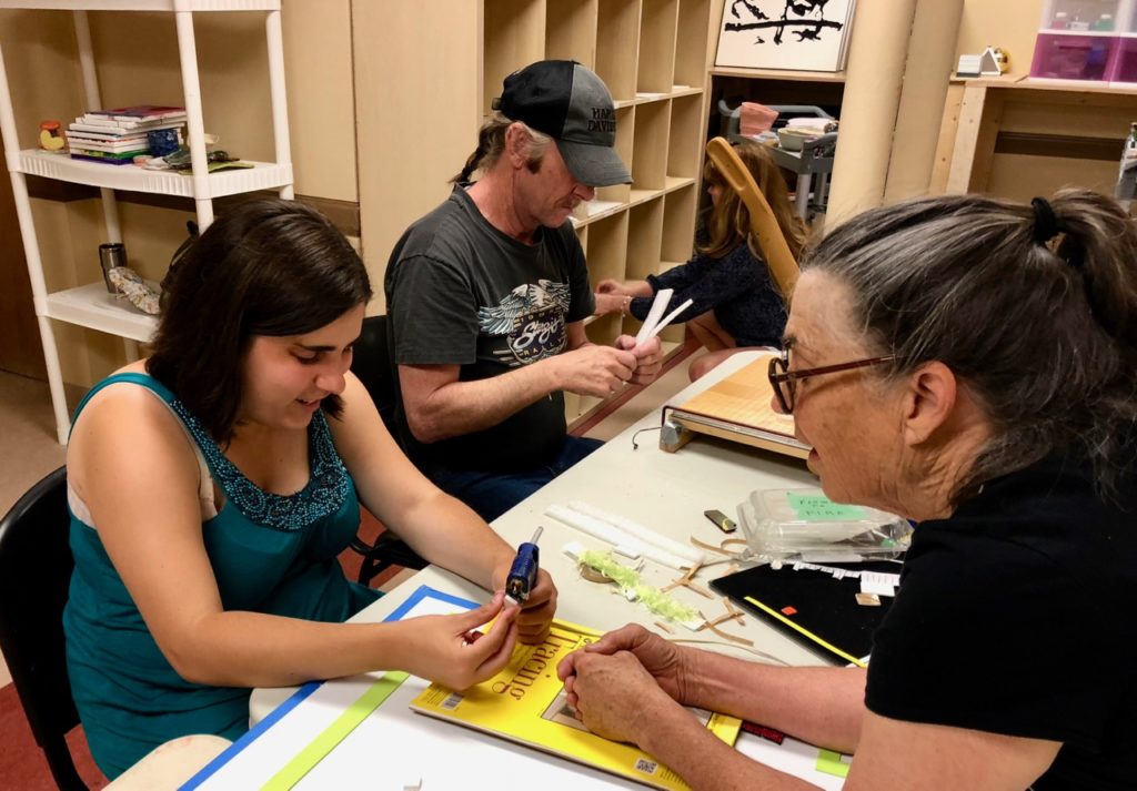 Danielle uses a hot glue gun for the 1st time, Ann Cunningham gives direction and in the background Brad uses the paper cutter