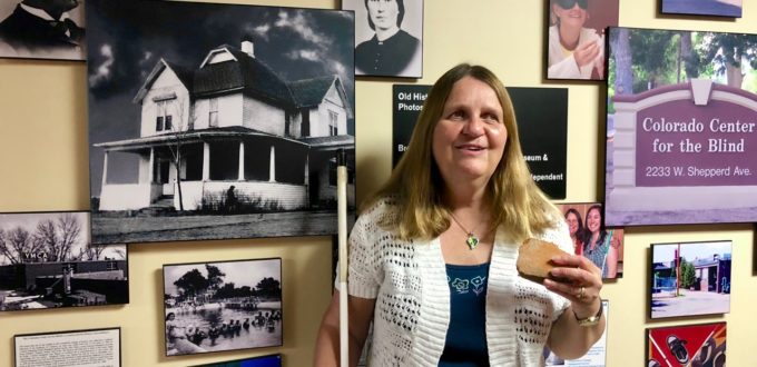 A smiling Julie holds a piece of broken red brick as she stands in front of a wall of black-and-white photos.