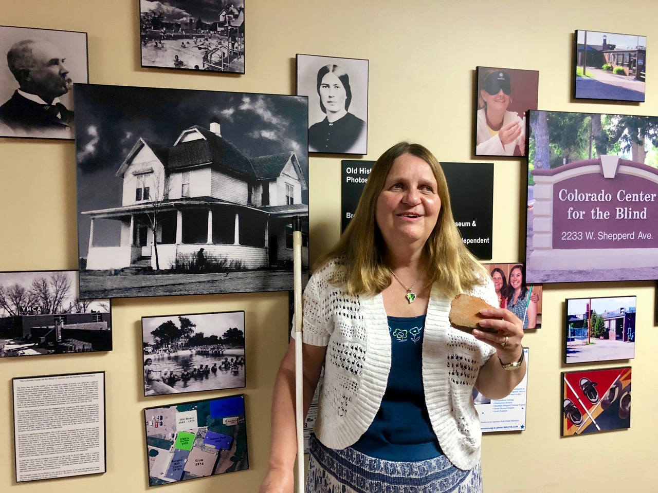 A smiling Julie Deden holds a piece of broken red brick as she stands in front of a wall of black-and-white photos.
