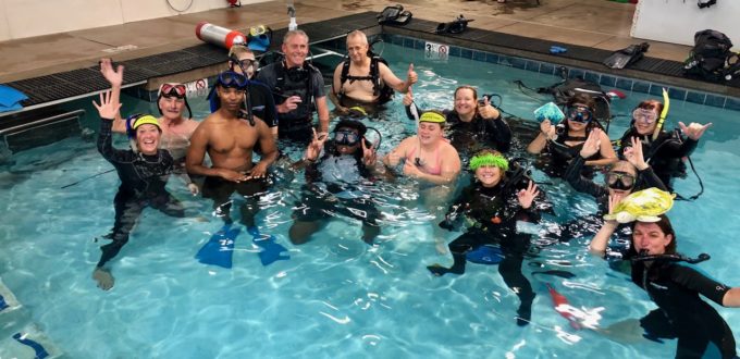 Group of 14 in Scuba Gear in the corner of the pool smile and wave