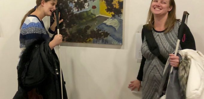 Jen looks at a tactile painting while Stefanie reads the Braille description