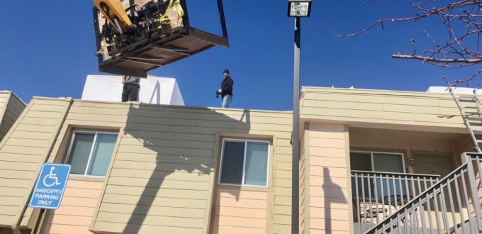 Roofing crew on top of the apartents with their snow blowers