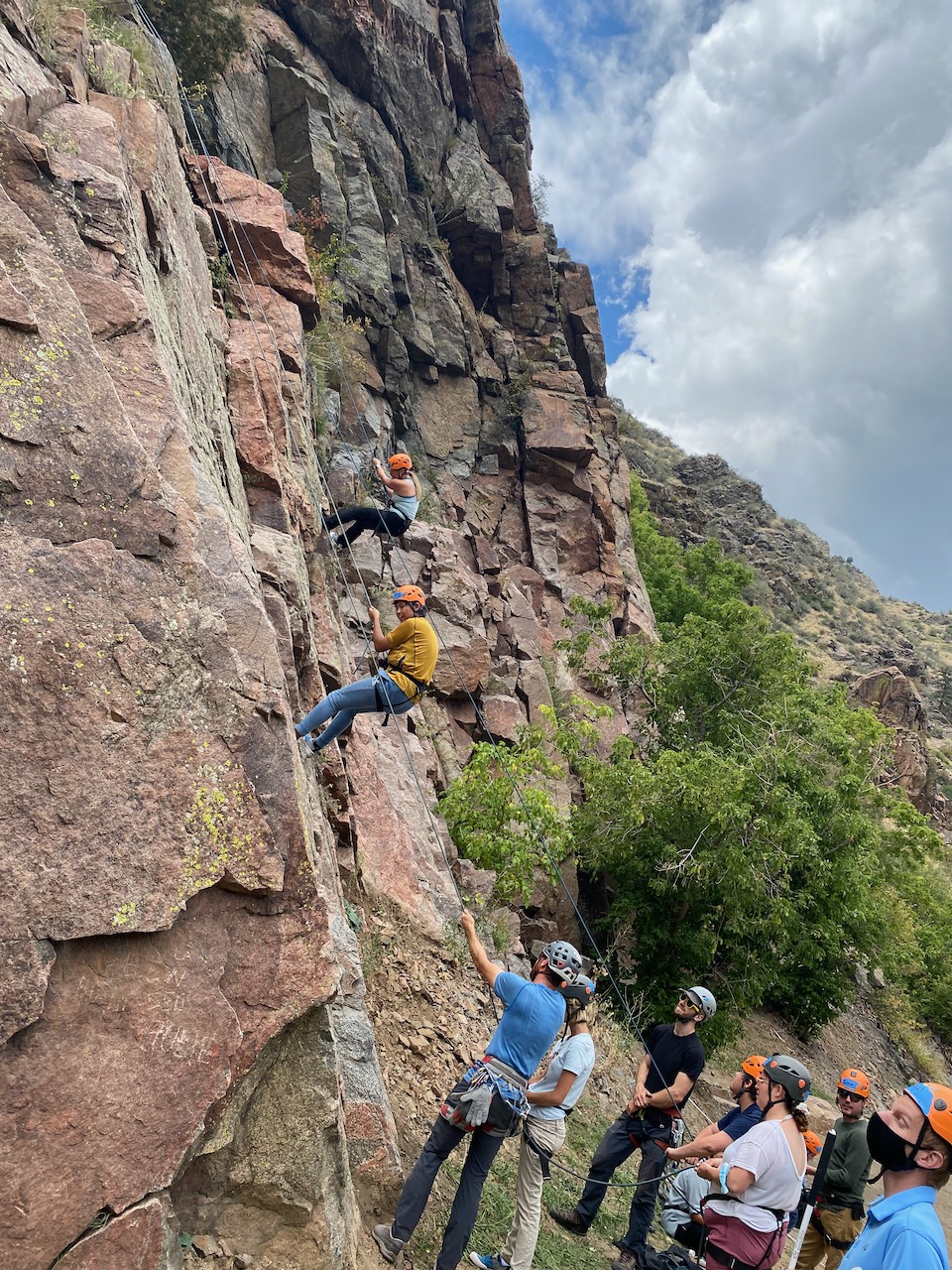Two female climbers shown on the rock while others look on from below